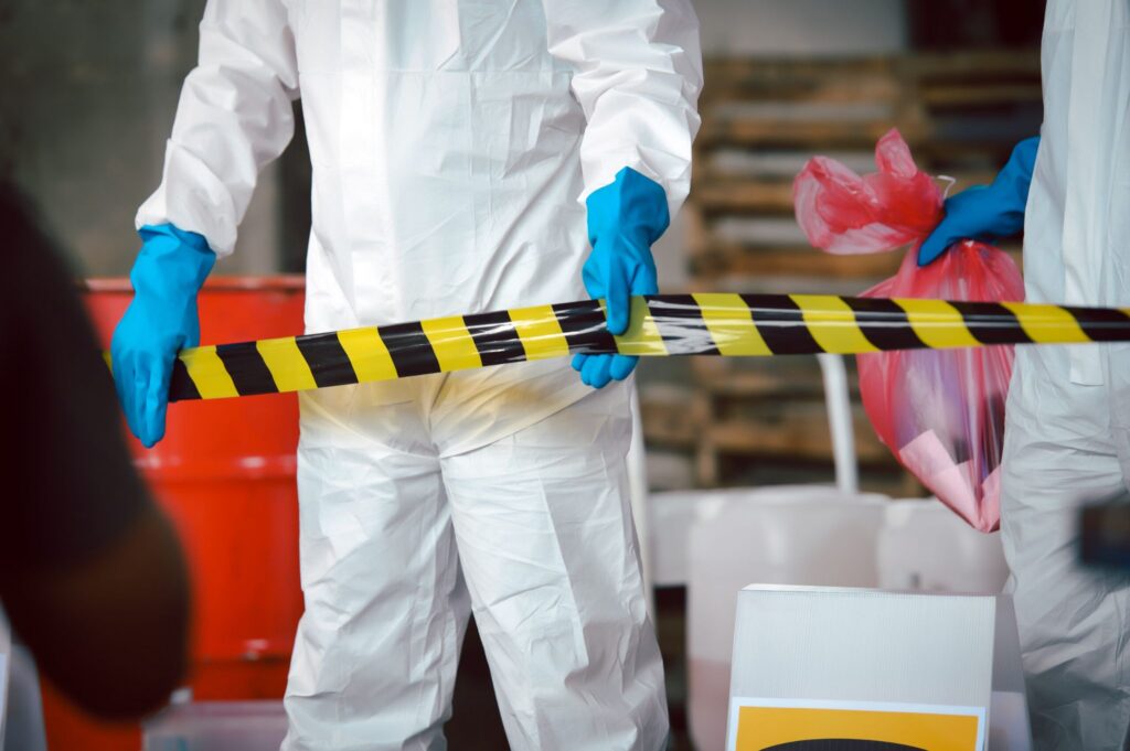Technicians in protective suits setting up caution tape and handling biohazard waste, highlighting professional biohazard cleanup services by Paul Davis Restoration of Mobile.